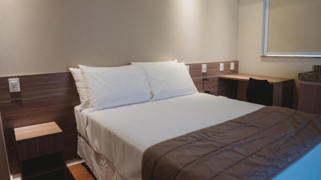 a bedroom with a bed with white sheets and pillows at Hotel Golden Inn Lafaiete in Conselheiro Lafaiete