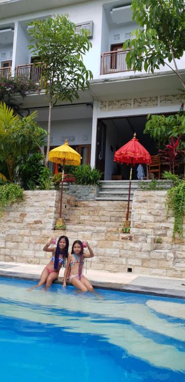 two girls are sitting in a swimming pool at Pondok Kembar Homestay in Uluwatu