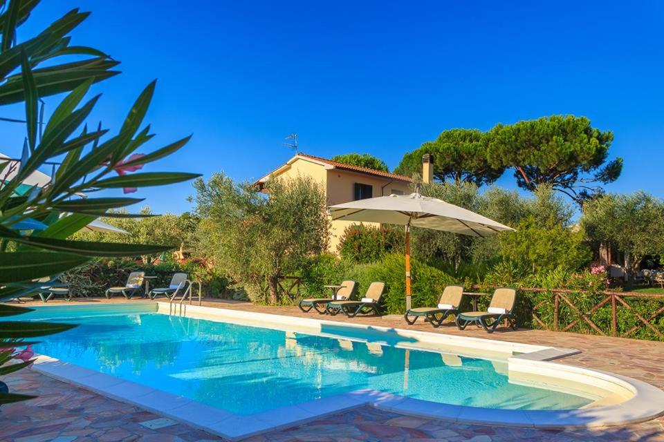 een zwembad met stoelen en een parasol naast een huis bij Agriturismo - B&B L'Acquacotta in Castiglione della Pescaia