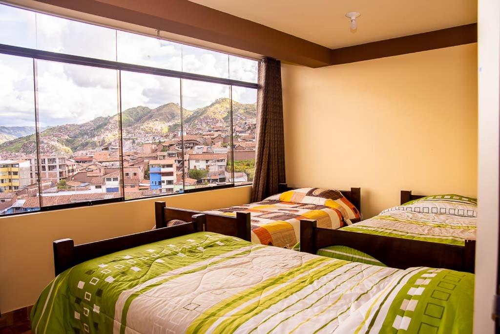 two beds in a room with a large window at Departamentos Santa Ana Barrio Tradicional in Cusco