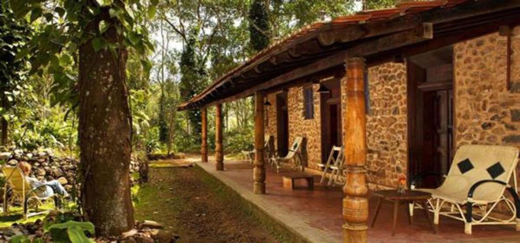 Cette maison en briques dispose d'une terrasse couverte avec des chaises. dans l'établissement Elephant Valley Eco Farm Hotel, à Kodaikānāl