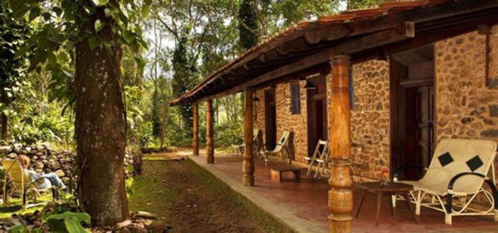 a brick house with a porch and chairs on a patio at Elephant Valley Eco Farm Hotel in Kodaikānāl