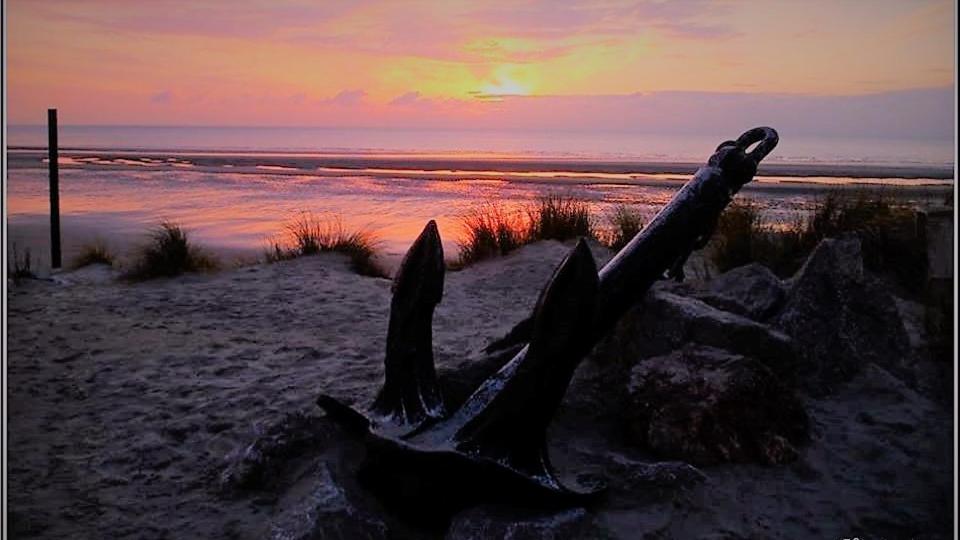 a beach with a sign in the sand at sunset at Maison de villégiature cote opale in Hardelot-Plage