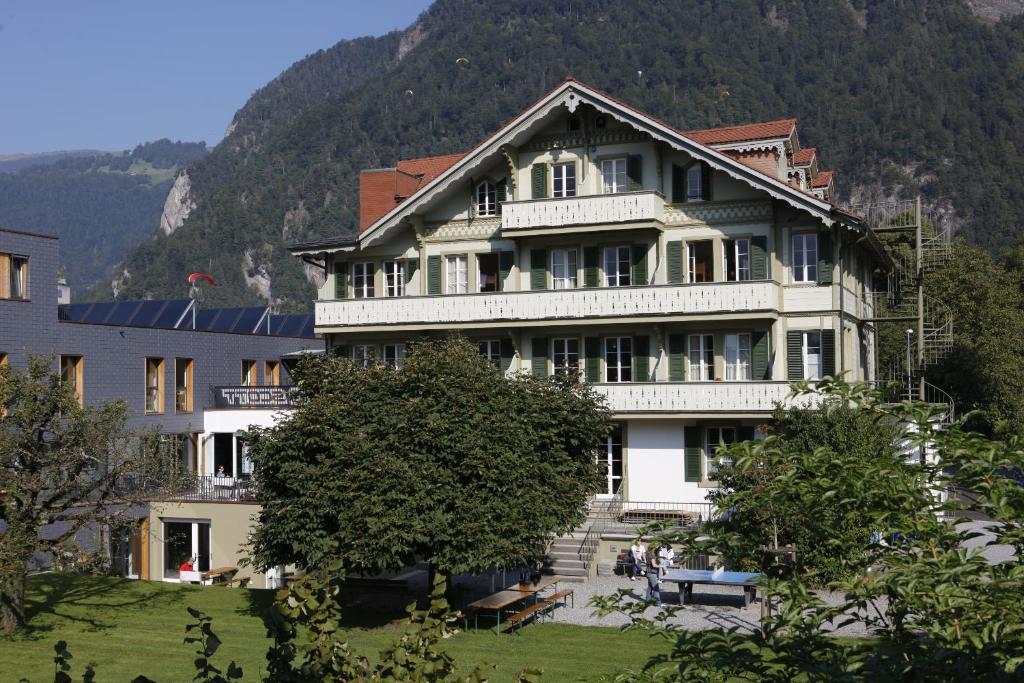 a large white building with stairs in front of a mountain at Chalet Hostel @ Backpackers Villa Interlaken in Interlaken