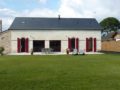 un grand bâtiment avec des portes rouges sur un champ vert dans l'établissement Jolie Maison de Campagne en pierre de tuffeau, à Longué