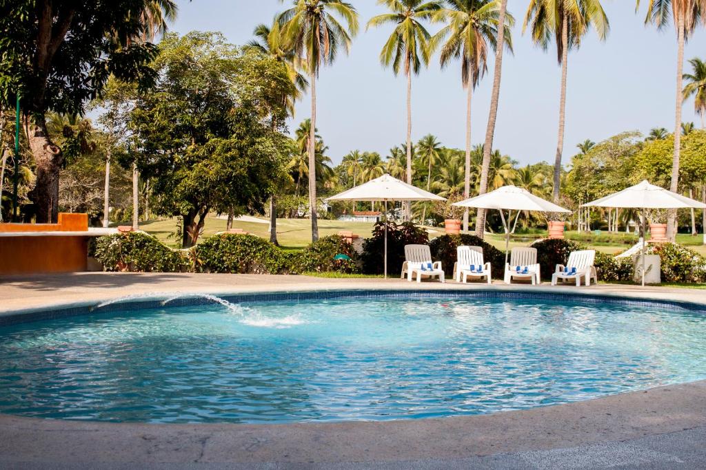 a swimming pool with chairs and umbrellas and palm trees at Coral Ixtapa in Ixtapa