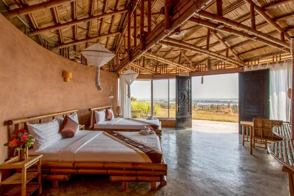 a bedroom with two beds and a large window at Hanchey Bamboo Resort in Kampong Cham