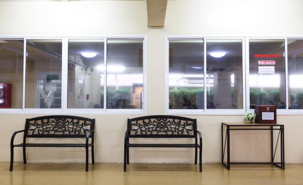 A covered communal seating area with two black benches beside interior windows.