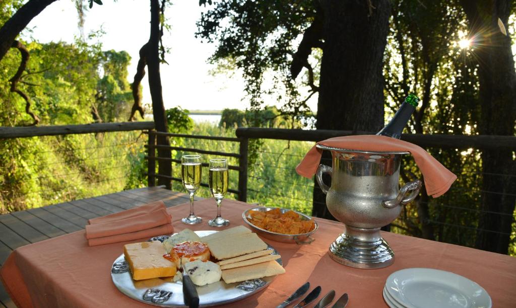 a table with a plate of food and glasses of wine at Chobe River Cottages in Kasane