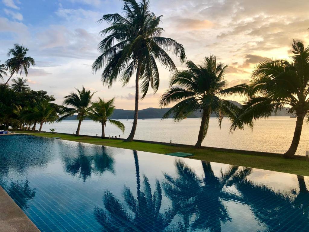una piscina con palmeras frente al océano en D-Lux 4 bed beachfront apartment with sea view, en Panwa Beach