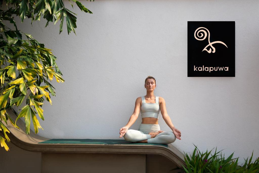 una mujer está sentada en una pose de meditación en un banco en Kalapuwa Resort, en Balapitiya