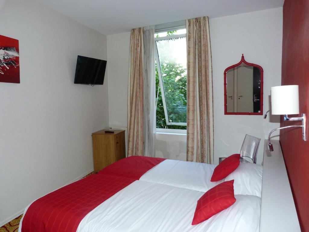 Un dormitorio con una cama con almohadas rojas y una ventana en Cit'Hotel Europeen en Angoulême