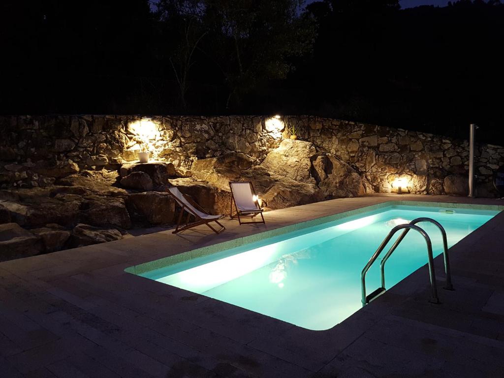 Cozy Villa Cristelo - Family & Friends في Cristelo: حمام سباحة في الليل مع أضواء على جدار حجري