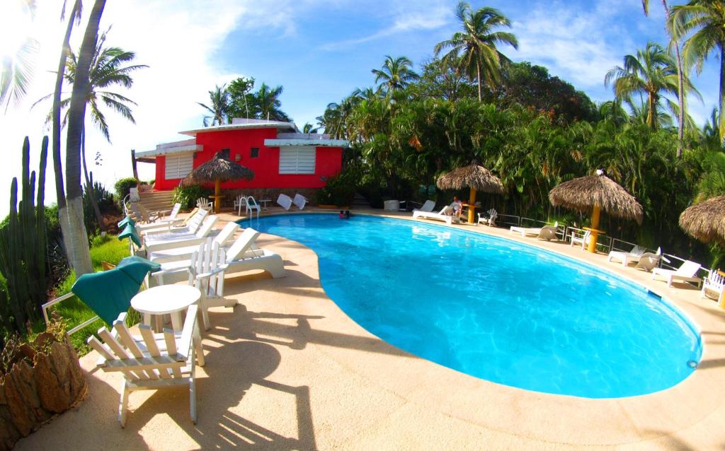 a swimming pool with white chairs and a red building at Hotel Flamingos in Acapulco