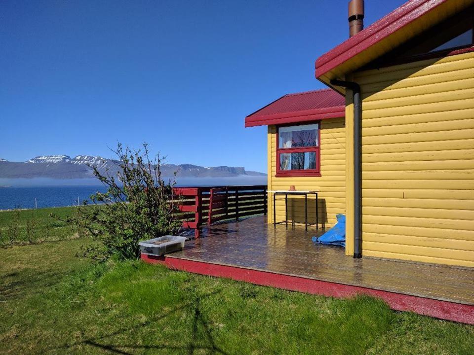 ein gelbes Haus mit einer Terrasse neben dem Wasser in der Unterkunft Gemlufall guesthouse in Þingeyri