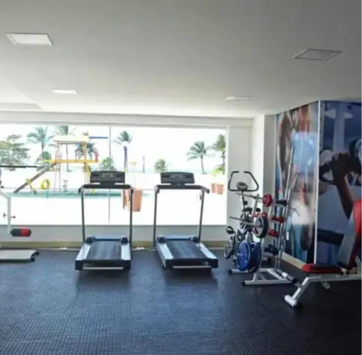 einen Fitnessraum mit mehreren Laufbändern und einem großen Fenster in der Unterkunft Condomínio Solaris residencial Club in Ilhéus