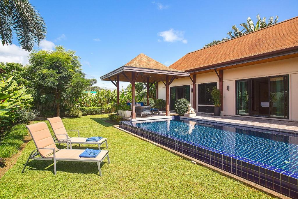 un patio trasero con piscina y 2 sillas junto a una casa en Kokyang Estate by TropicLook, en Nai Harn Beach