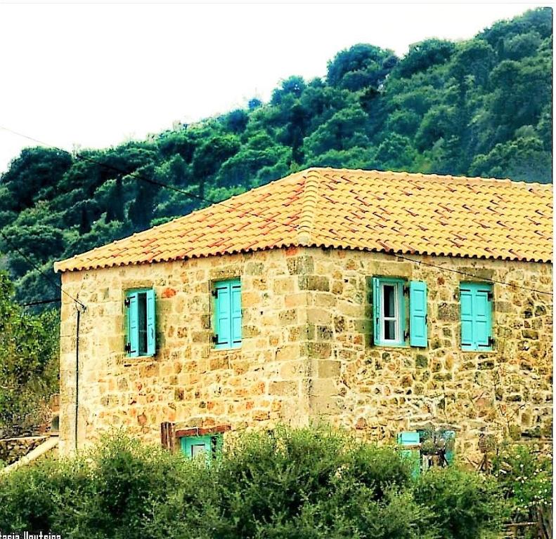 une maison en pierre avec des fenêtres bleues en face d'une montagne dans l'établissement The House. Light & Stone., à Lixouri