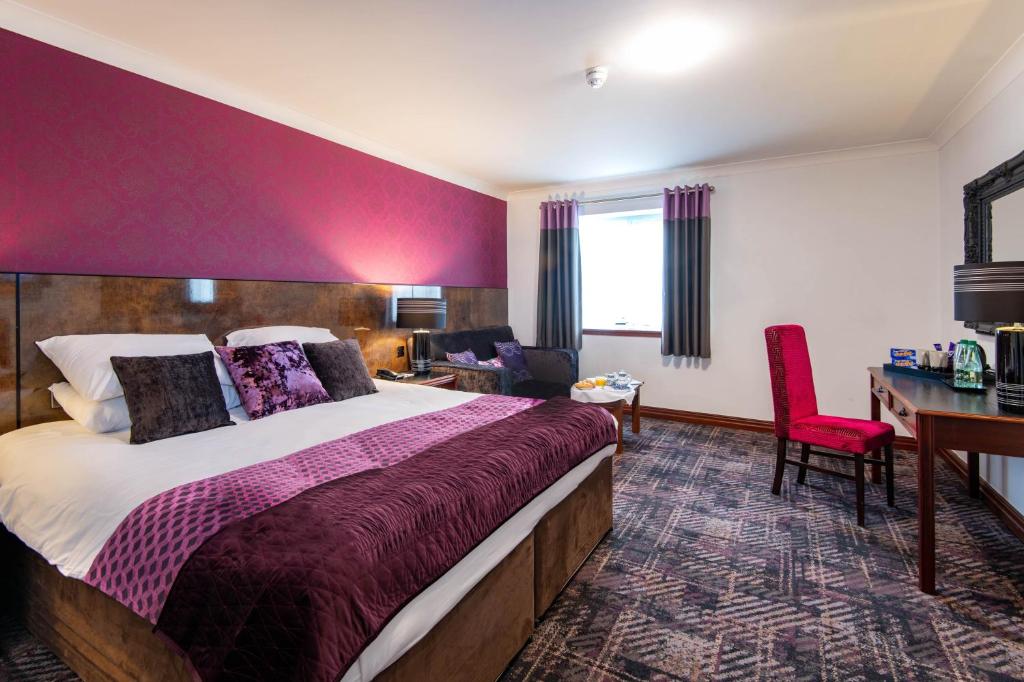オールダムにあるThe Victoria Hotel Manchester by Compass Hospitalityの大きなベッドとデスクが備わるホテルルームです。