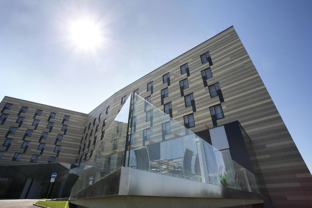 a building with a glass facade with the sun in the sky at Quality Hotel Ostrava City in Ostrava