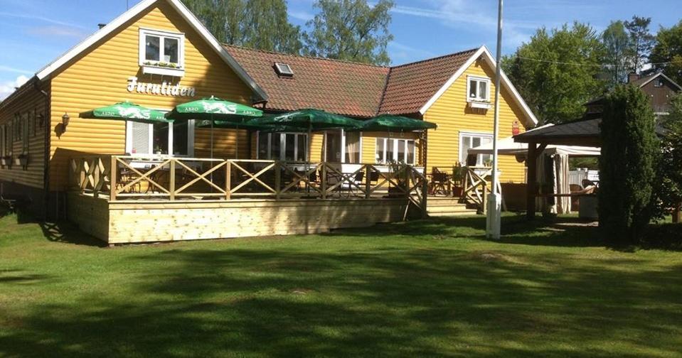 a yellow building with a restaurant with green umbrellas at Furulidens Hotell in Vittsjö