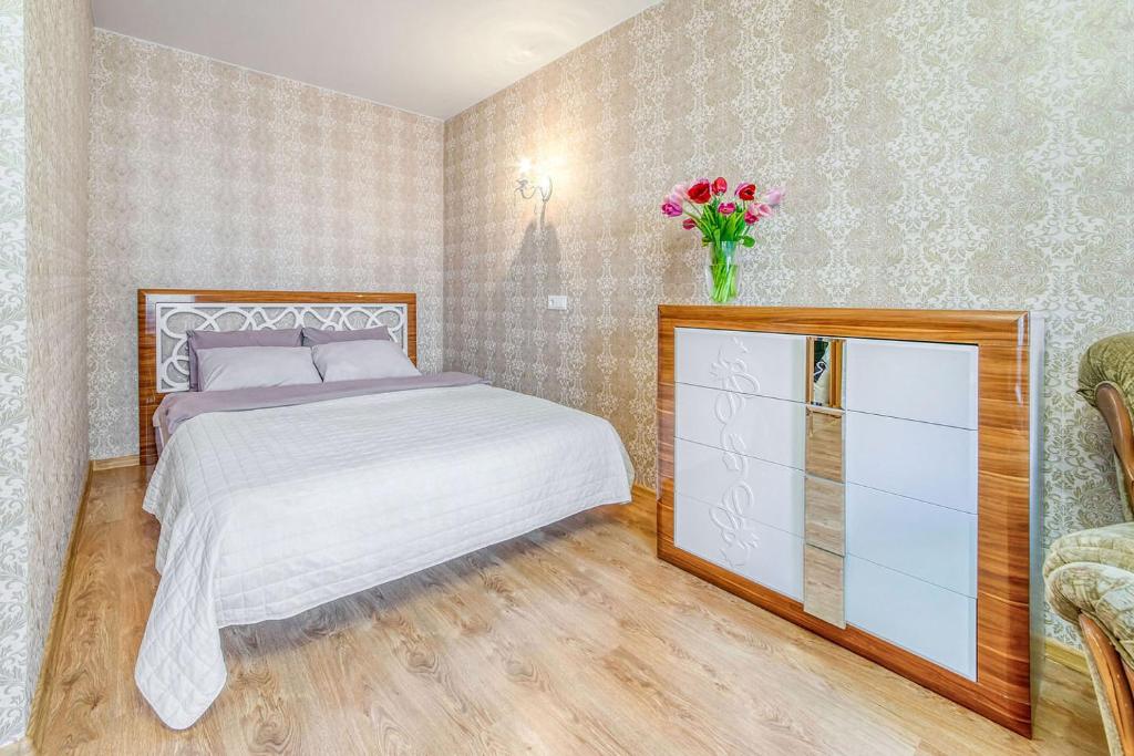 Helen Apartments Galleria Minsk في مينسك: غرفة نوم بسرير و إناء من الزهور