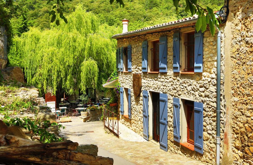 uma casa de pedra com janelas azuis e uma árvore em Hostellerie du Vieux Moulin em Duilhac