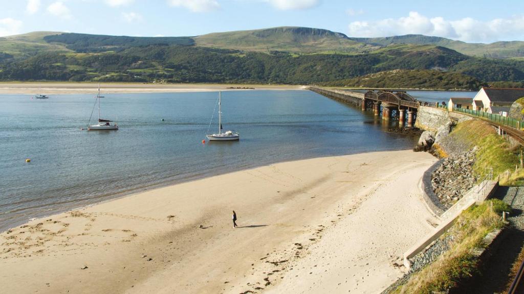 Llanddwyweにある92 Barmouth Bay Holiday Parkの海に浮かぶ船を持つ浜辺に立つ男