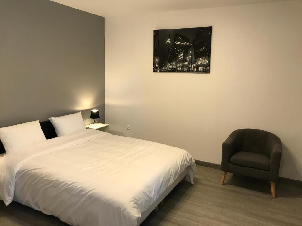 um quarto com uma cama branca e uma cadeira em Studio Gallieni em La Châtre