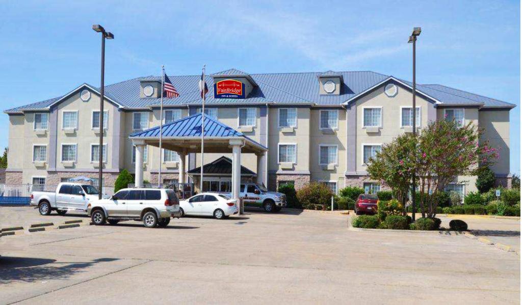 un gran hotel con coches estacionados en un estacionamiento en FairBridge Inn & Suites Cleburne, en Cleburne