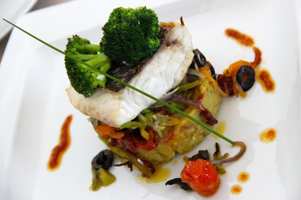 a white plate with a piece of fish and broccoli at Martinhal Sagres Beach Family Resort Hotel in Sagres
