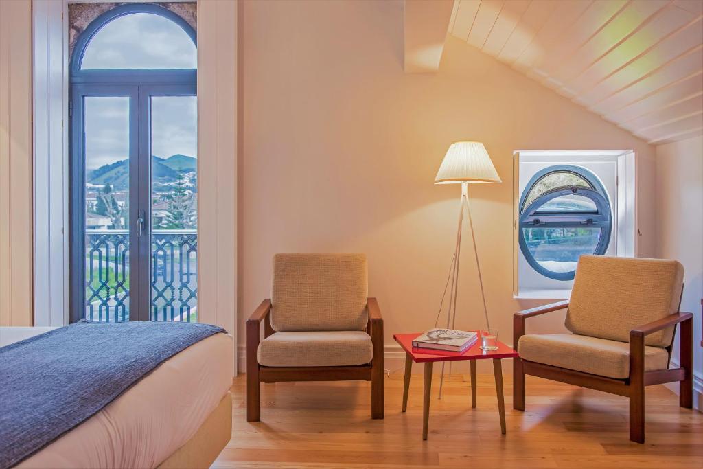 a bedroom with a bed and two chairs and a table at Herdade do Ananás in Ponta Delgada