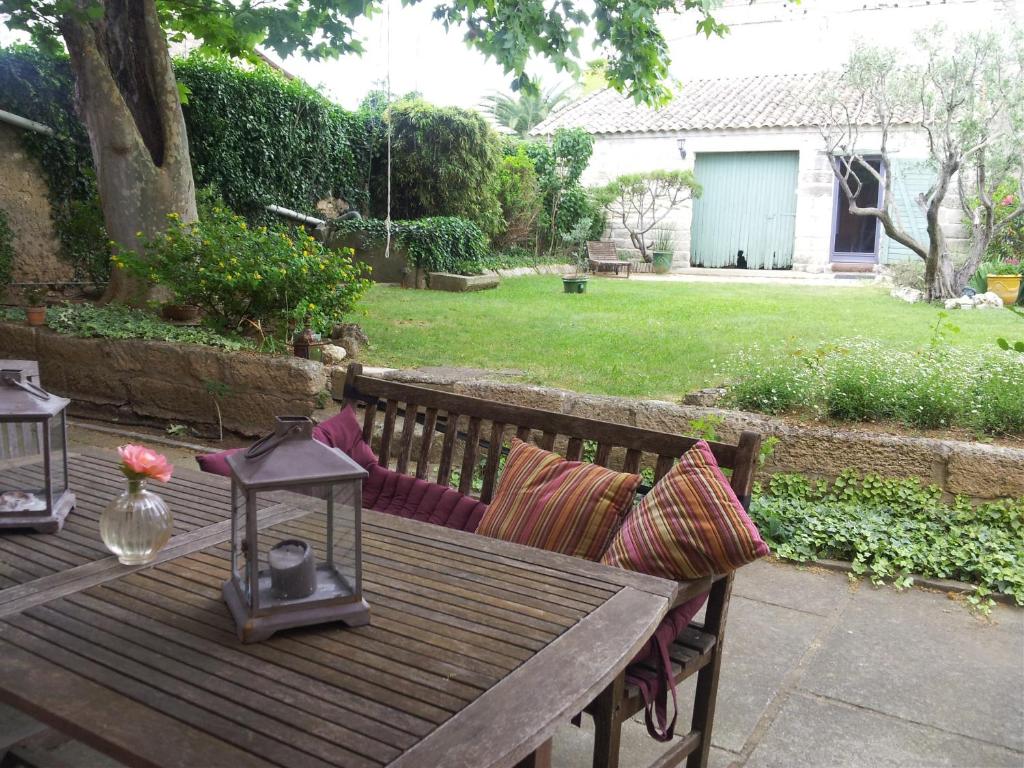 a wooden bench with pillows and a table in a yard at Chambres de charme chez l'habitant in Baillargues