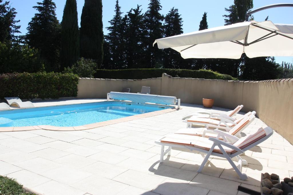 a swimming pool with two chairs and an umbrella at Loft du moulin de Milan in Cheval-Blanc