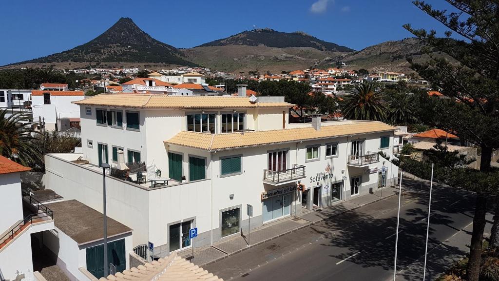 a large white building with mountains in the background at Sotavento Guest House in Porto Santo
