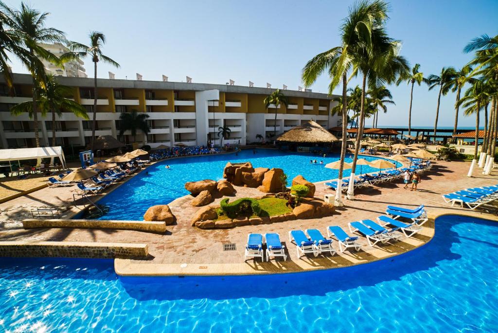 un complejo con una gran piscina, sillas y palmeras en El Cid Castilla Beach en Mazatlán