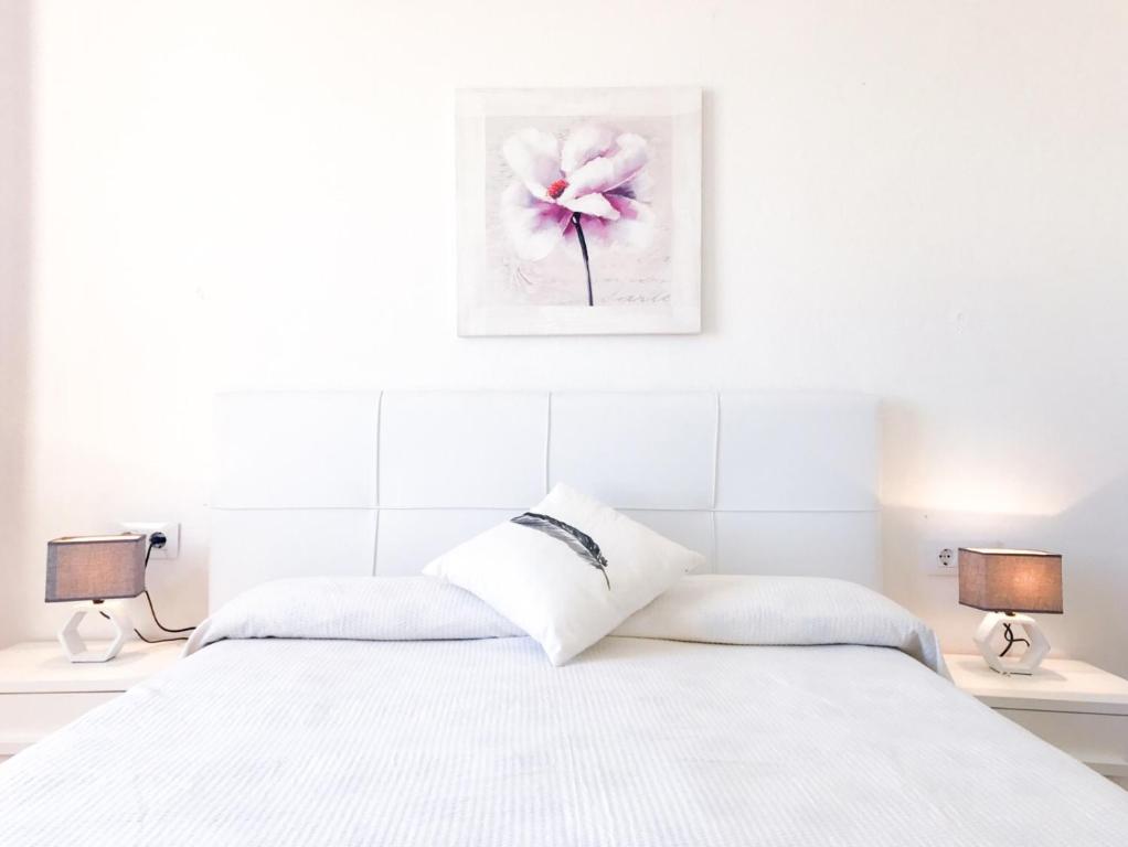 a white bedroom with a white bed with two lamps at Vistas al mar y la piscina in Arenal d'en Castell