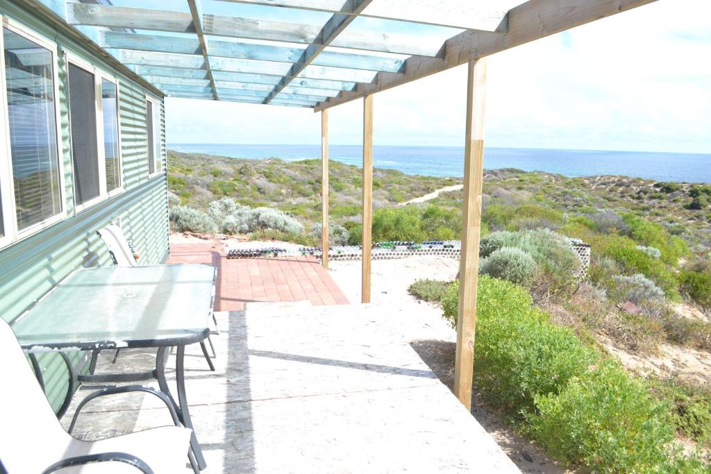 un porche con mesa, sillas y el océano en Private Beach Cottage At Ecostays, en Greenough