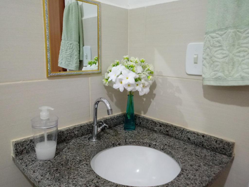 a bathroom sink with a vase of flowers on it at Casa Aeroporto Maceió in Maceió