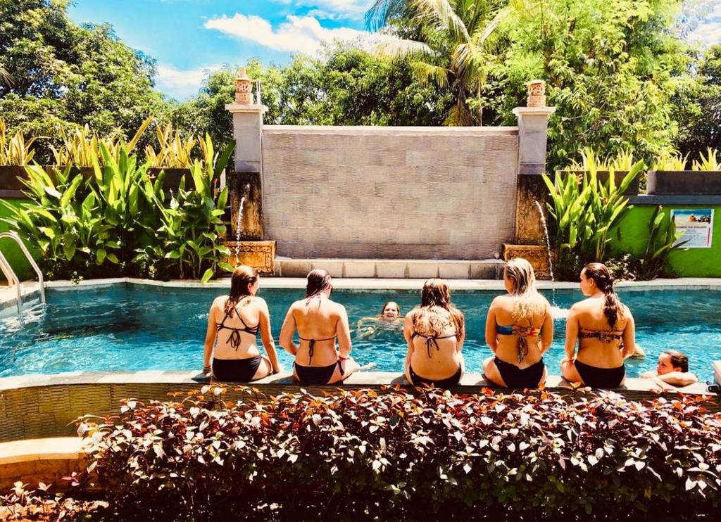a group of women in bikinis sitting around a swimming pool at Lembongan Hostel in Nusa Lembongan