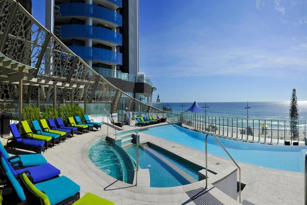 a swimming pool with chairs and the ocean in the background at Soul - Private Apartments - Apartment Stay in Gold Coast
