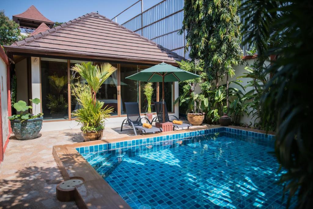 a swimming pool with an umbrella next to a house at Pratumnak Soi 5 Bungalow 3 in Pattaya South