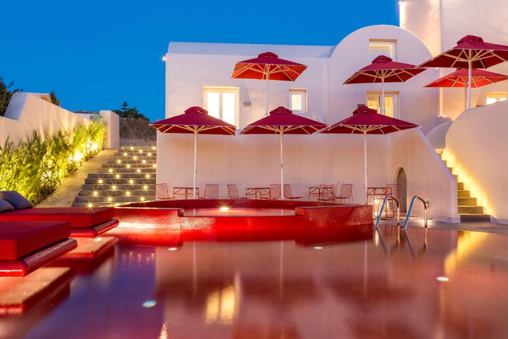 einem Pool mit roten Sonnenschirmen vor einem Gebäude in der Unterkunft Art Hotel Santorini in Pirgos