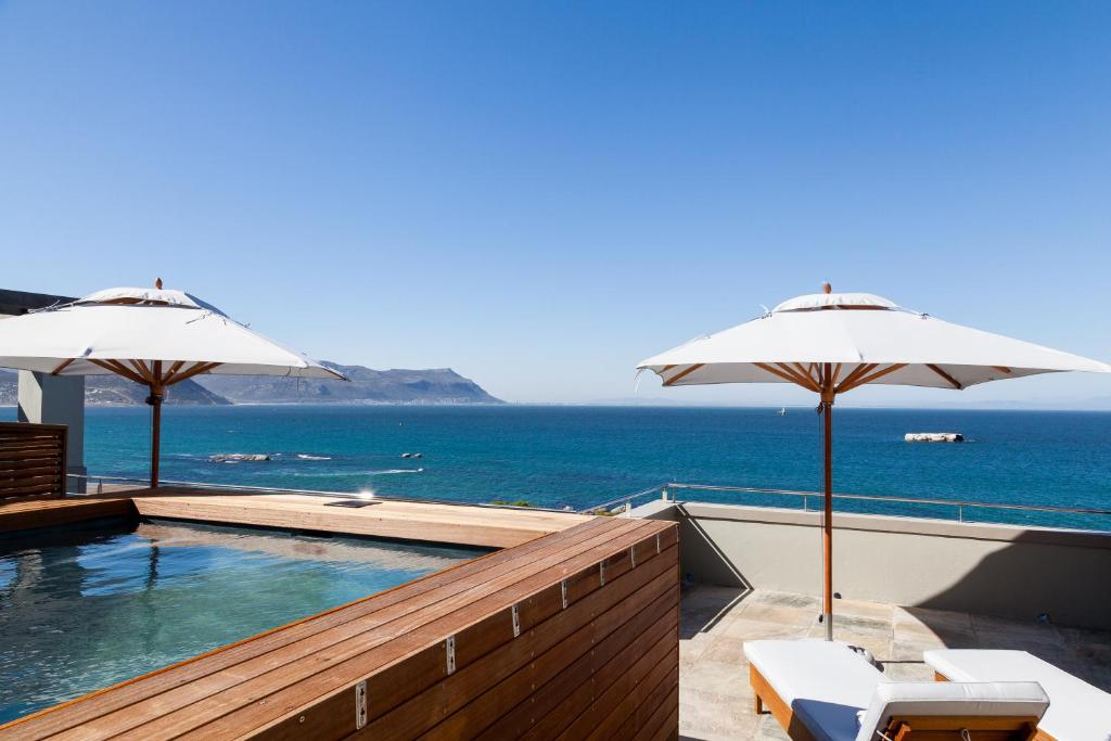 a swimming pool with two umbrellas and the ocean at Tintswalo Boulders in Simonʼs Town