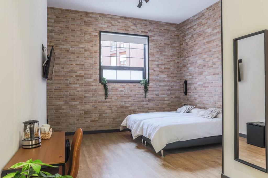 ein Schlafzimmer mit einer Ziegelwand, einem Bett und einem Tisch in der Unterkunft Pensión H30 Bilbao in Bilbao