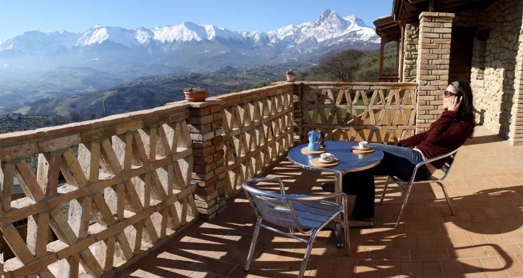 una donna seduta a un tavolo su un balcone con montagne di B&B Scacciapensieri - Vini d'Altura a Colledara