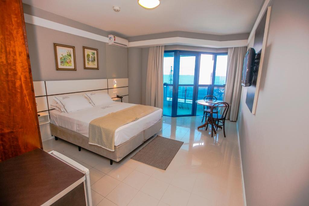 a bedroom with a bed and a table and a balcony at Hotel Bhally in Balneário Camboriú