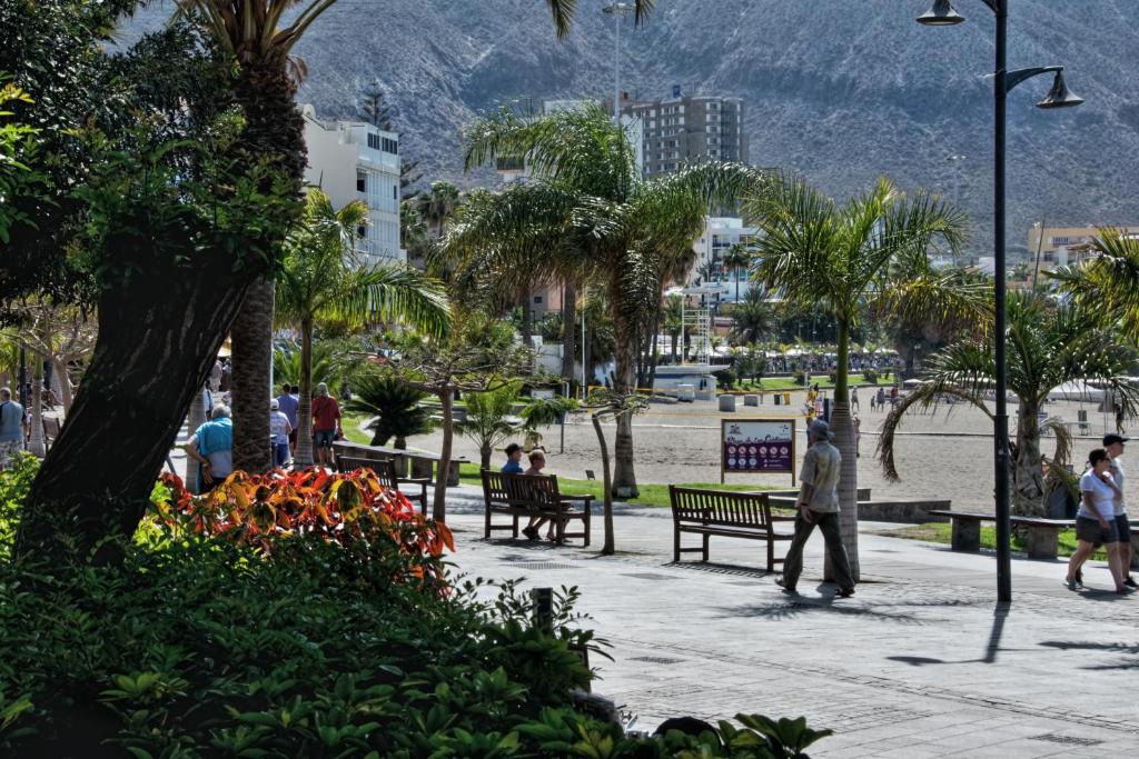 Gente caminando y sentada en bancos en un parque en EMMA - Los Cristianos, en Los Cristianos