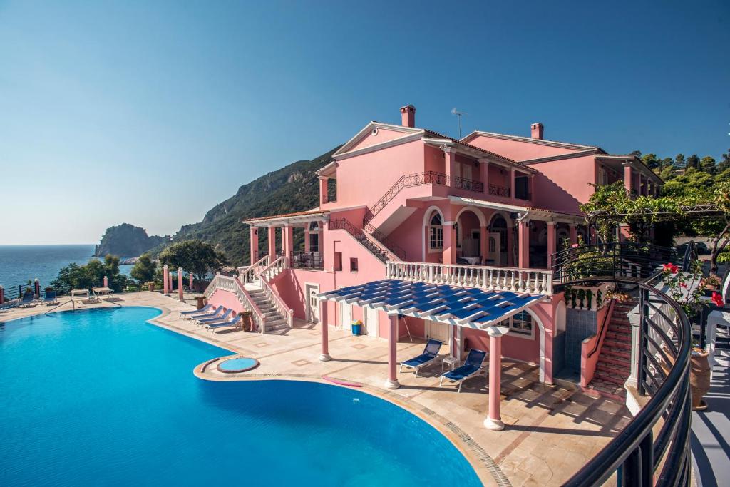 een roze huis met een zwembad aan de oceaan bij Hotel Elena Ermones in Ermones