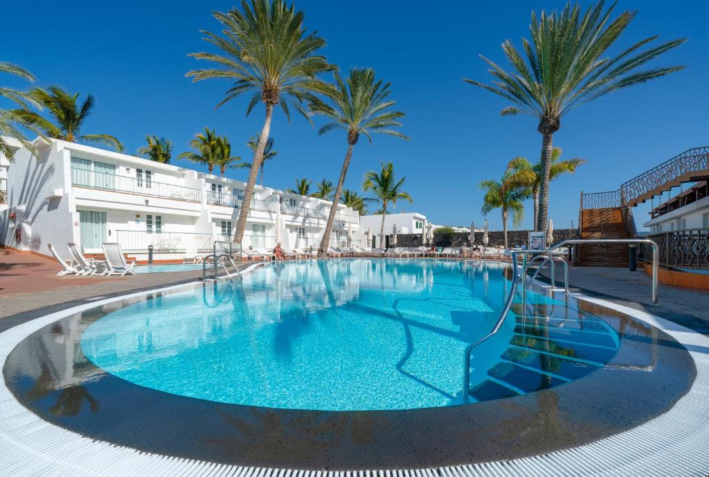 een groot zwembad met palmbomen voor een gebouw bij Plus Fariones Apartamentos in Puerto del Carmen